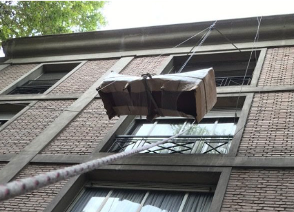 Caja izada con una cuerda en el exterior de un edificio de ladrillos con ventanas.