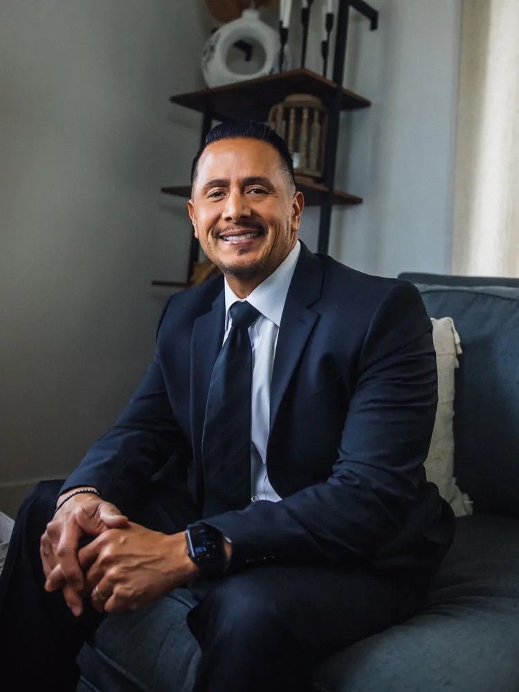 Allen Splopuko, AMS Law A man in a suit and tie is sitting on a couch.