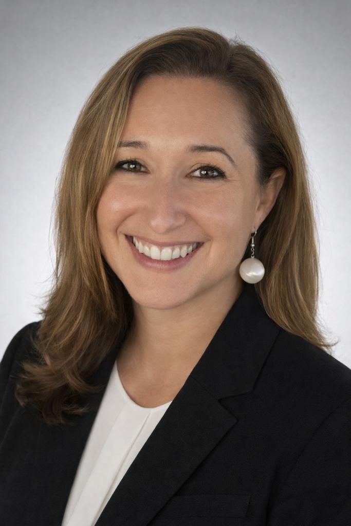Woman smiling, wearing a black blazer and white shirt, pearl earrings.