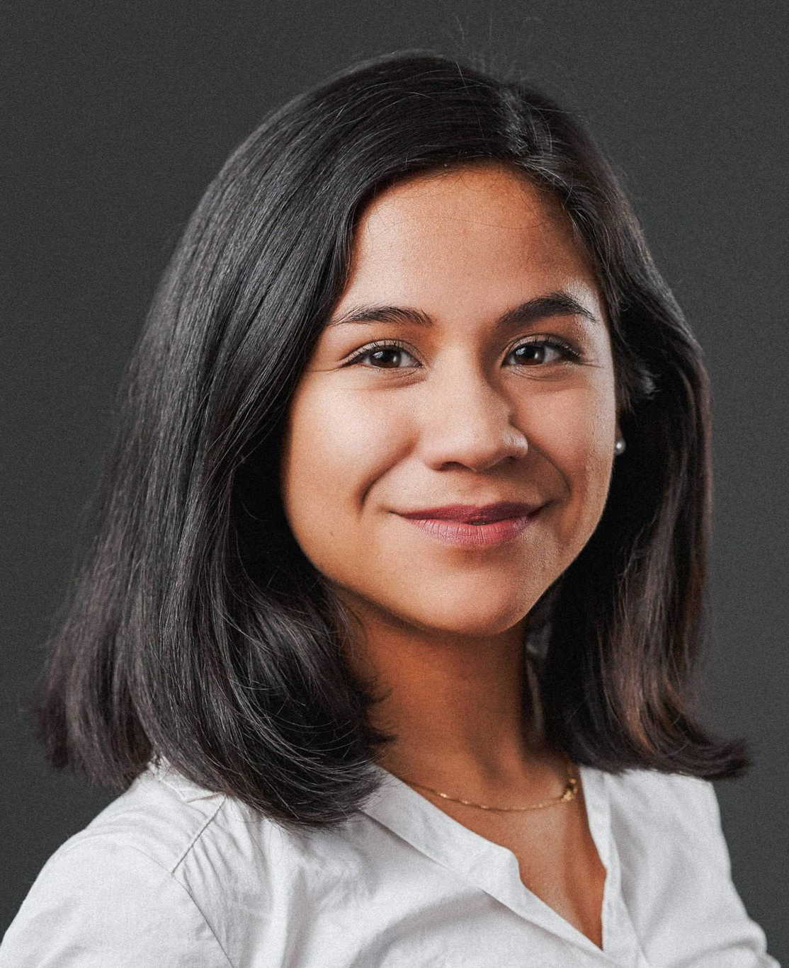 Clarissa Calderon Portrait of a smiling woman with shoulder-length dark hair wearing a white blouse against a gray background