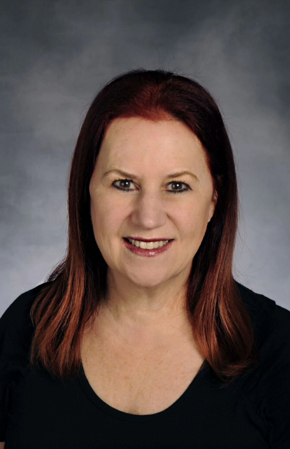 Donna Gurr Woman with reddish-brown hair smiling, wearing a black shirt, against a gray background.
