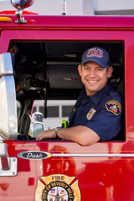 Firefighter in uniform smiling inside red fire truck, City of Beverly Hills.