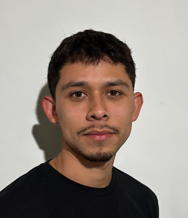 Man with short dark hair and a thin mustache, wearing a black shirt, looking directly at the camera.