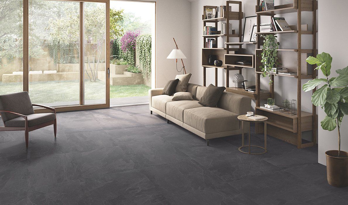 Soggiorno moderno con divano grigio, scaffali e grandi porte finestre che si aprono su un giardino.
