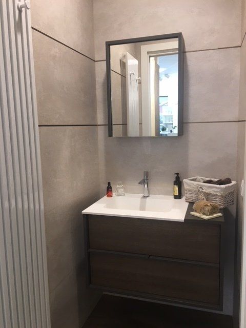 Mobile bagno moderno con specchio, lavabo, dispenser di sapone e cestino sul lato destro.