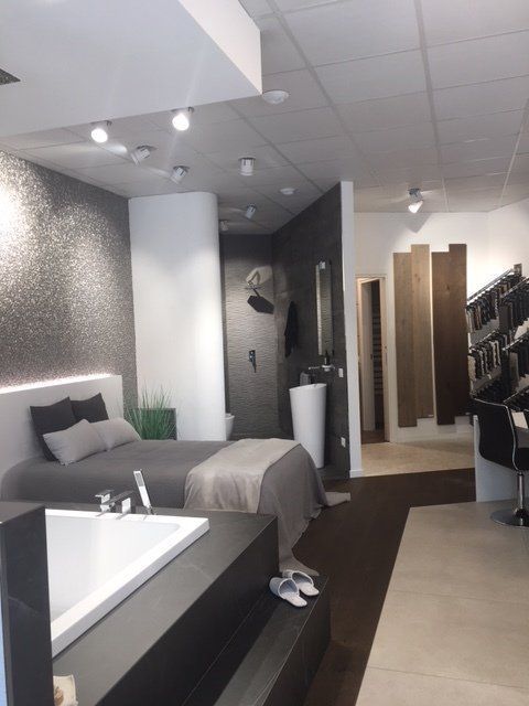 Camera da letto moderna in stile showroom con letto grigio, vasca bianca, dettagli in legno e appendiabiti.