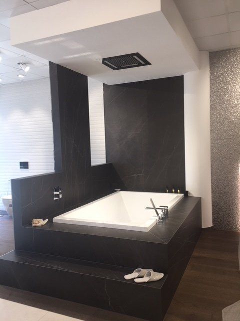 Bagno moderno con una grande vasca da bagno nera, rivestimento bianco e pareti rivestite con piastrelle scure.