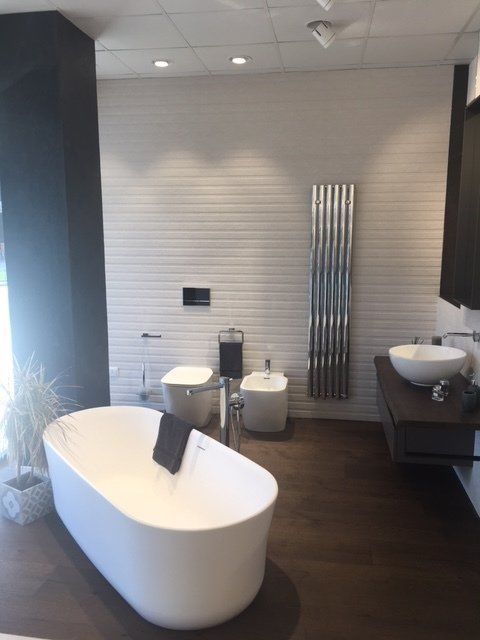 Bagno moderno con vasca freestanding, lavabo bianco, pavimento in legno scuro e scaldasalviette cromato.
