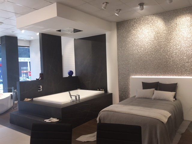 Showroom di camere da letto moderne con due letti in legno scuro, biancheria da letto grigia e pareti con finitura materica.