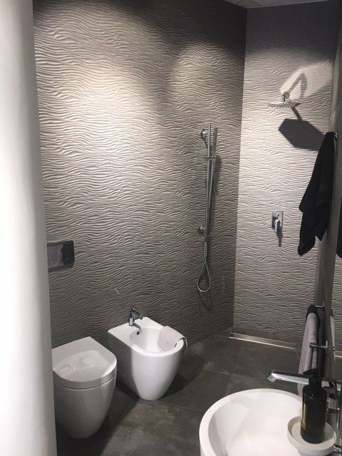 Bagno moderno con pareti grigie texturizzate, bidet, WC, doccia, lavabo e portasciugamani.