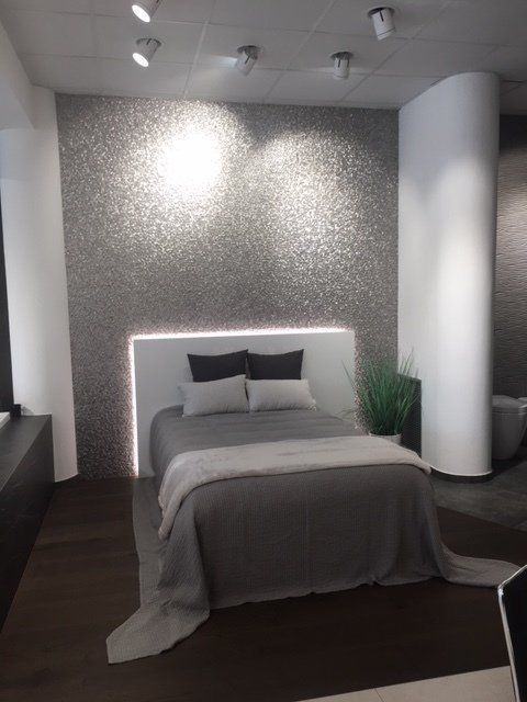 Camera da letto moderna con letto grigio, testiera retroilluminata, parete decorativa con texture e pavimento in legno scuro.