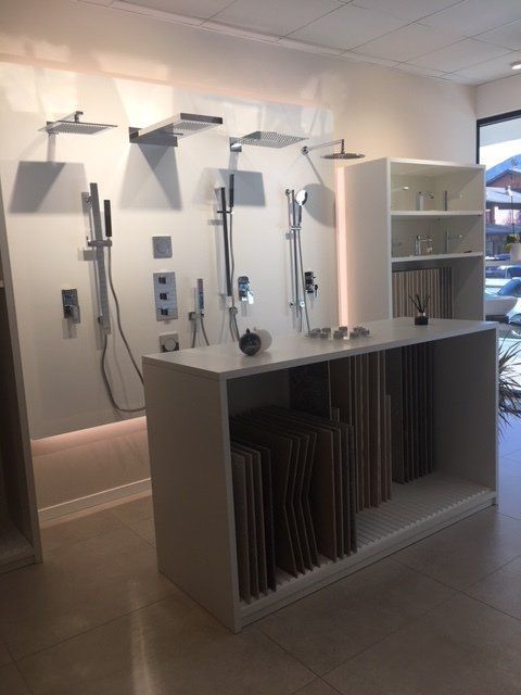 Esposizione di bagni in stile showroom con moderni accessori per la doccia, mensole e un armadietto con campioni di piastrelle.