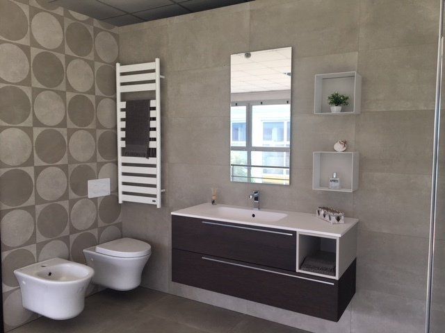 Bagno moderno con mobile lavabo sospeso, specchio, vasca bianca e bidet, su pareti rivestite con piastrelle grigie.