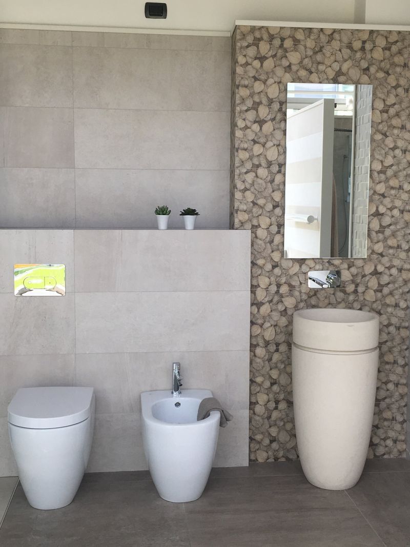 Bagno moderno con sanitari bianchi, grandi piastrelle in pietra a parete e uno specchio sopra un lavabo a colonna.