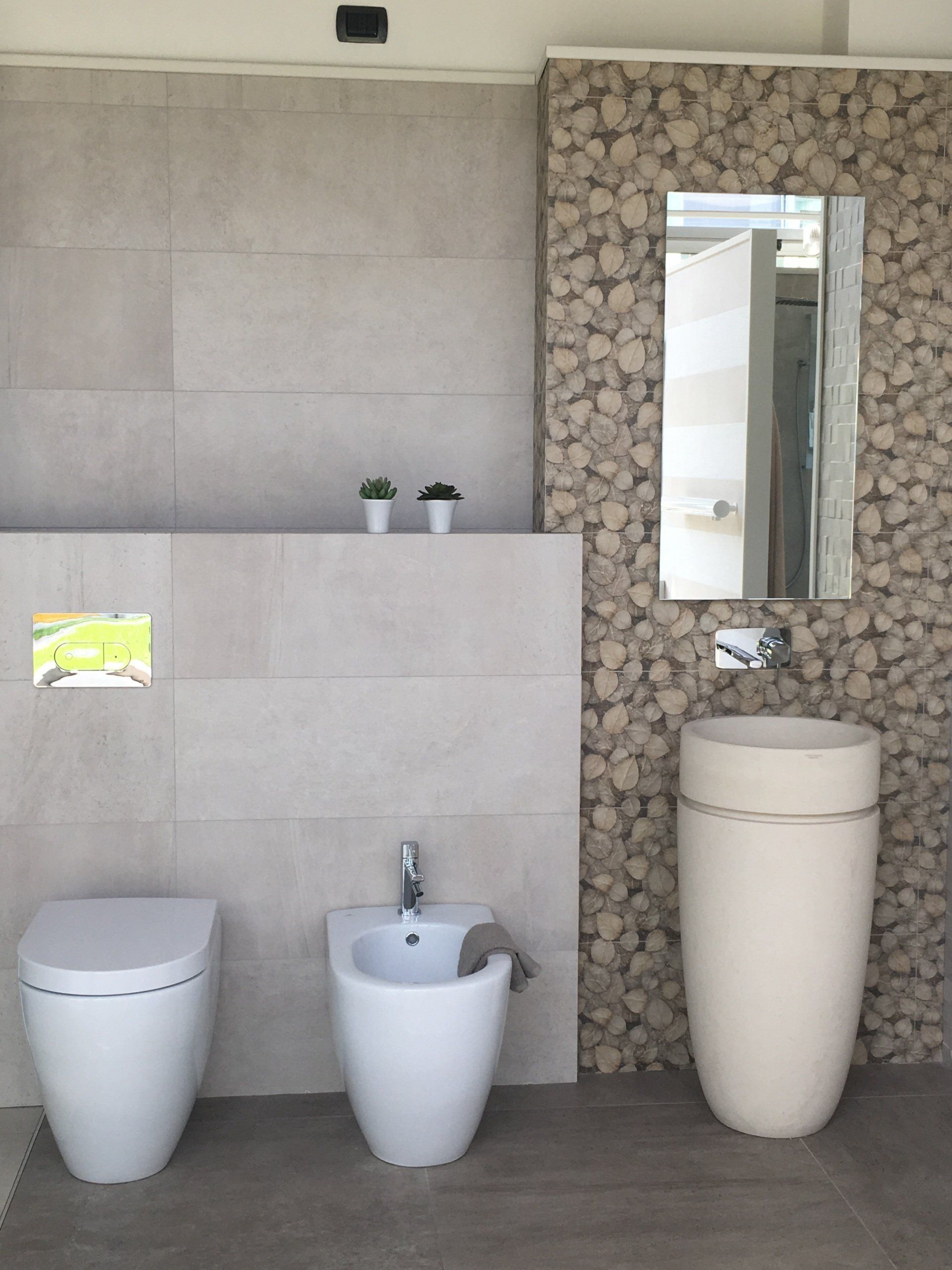 Bagno moderno con due WC, un bidet e un lavabo alto a forma di vaso, incastonato in pareti rivestite di piastrelle e pietra.