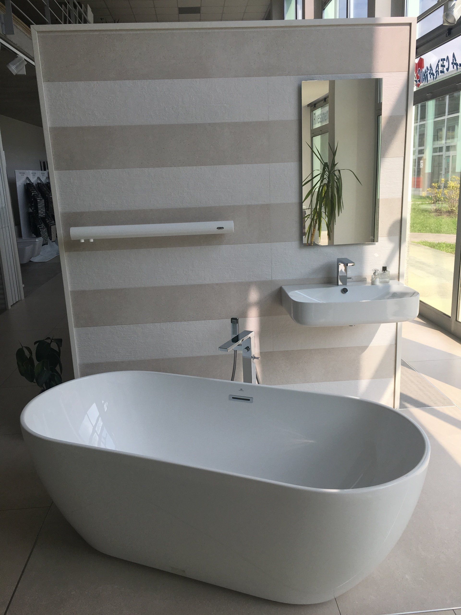 Bagno moderno con vasca bianca freestanding, lavabo a parete, specchio e rivestimento a parete con piastrelle a righe.
