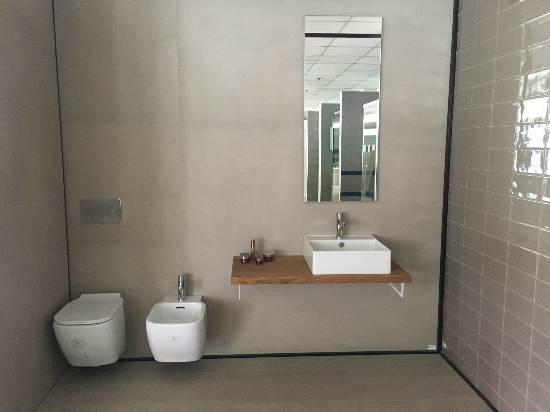 Bagno moderno e minimalista con WC, bidet, lavabo sospeso e specchio a parete su pareti rivestite con piastrelle beige.