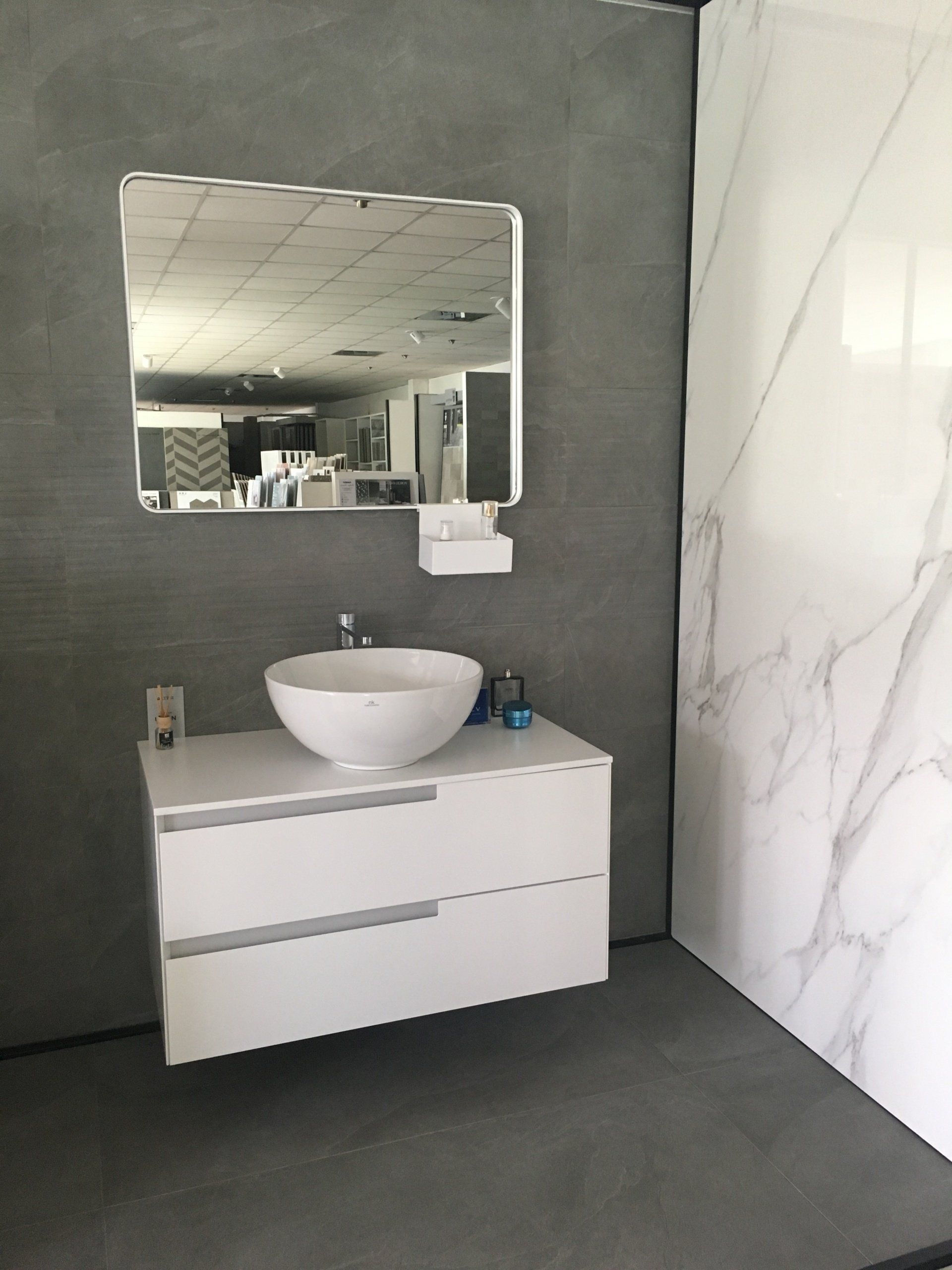Mobile bagno moderno con lavabo bianco, specchio, parete grigia e piastrelle decorative effetto marmo.