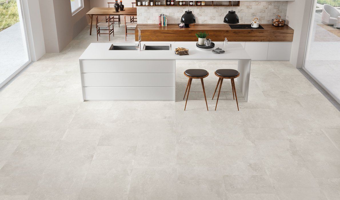 Cucina moderna e luminosa con isola bianca, due sgabelli e bancone posteriore con inserti in legno.