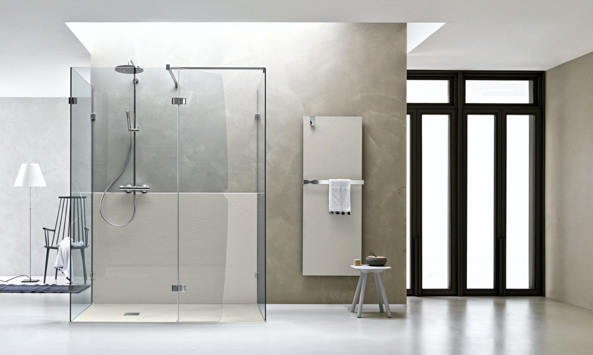 Bagno moderno e minimalista con doccia in vetro, termosifone a parete, sgabello e ampia finestra.