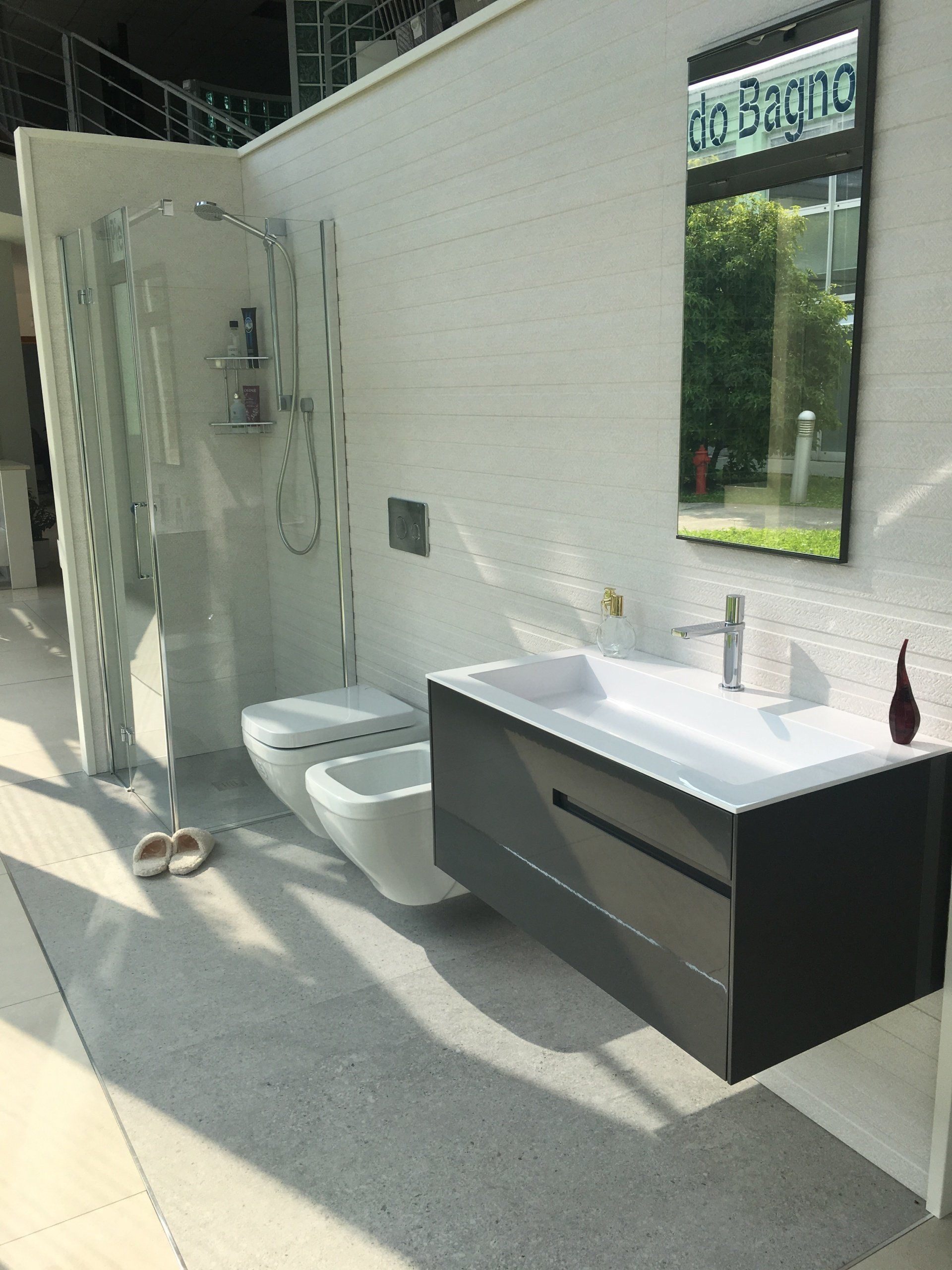 Bagno moderno con WC bianco, lavabo con mobiletto grigio, ampio specchio e box doccia in vetro.