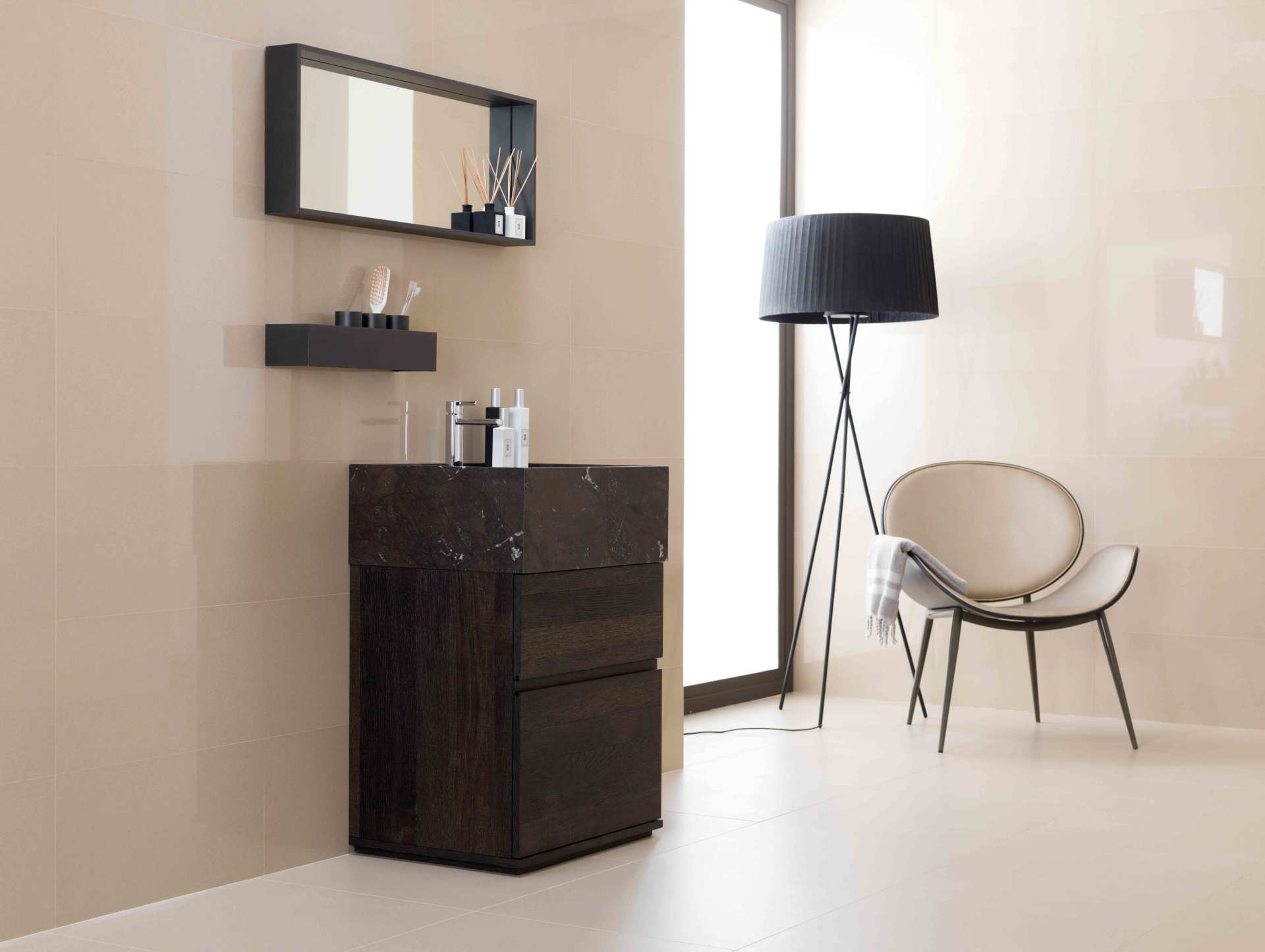 Bagno moderno e minimalista con mobile lavabo scuro, specchio, mensola, sedia e lampada da terra accanto a una finestra luminosa.