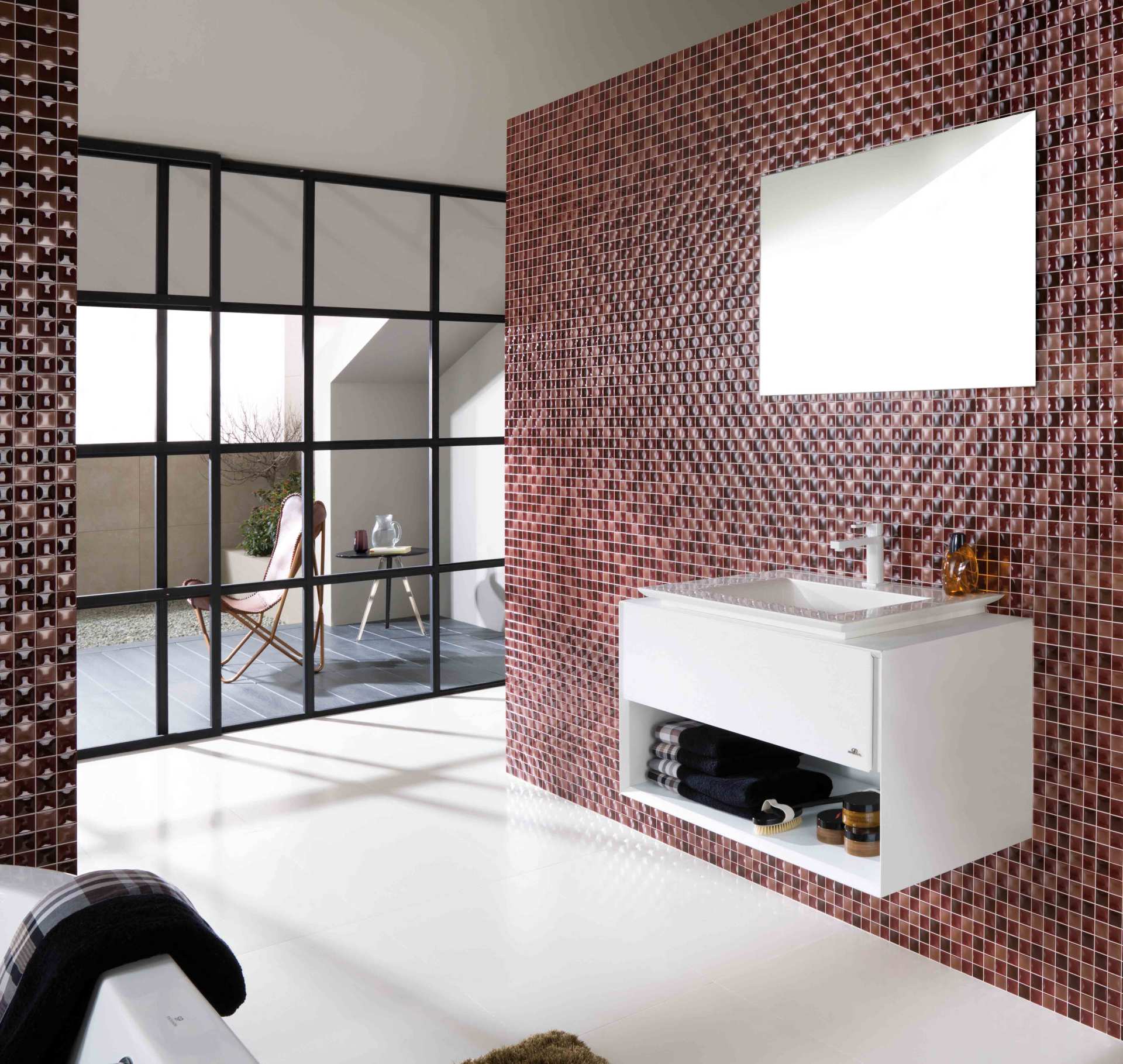 Bagno moderno con parete decorata con motivi rossi, mobile lavabo bianco, specchio e parete divisoria in vetro con cornice nera verso la stanza adiacente.