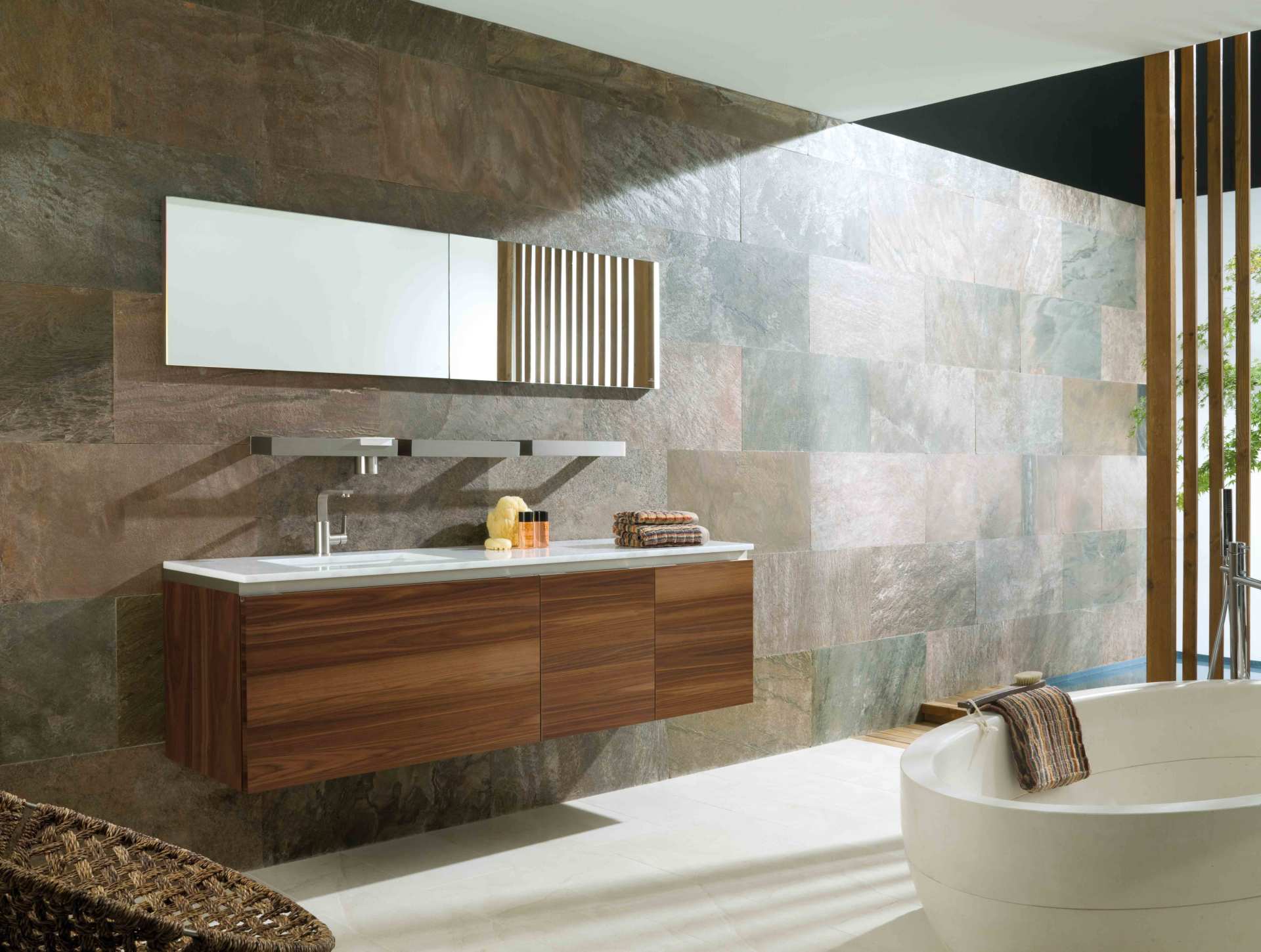 Bagno moderno con mobile lavabo sospeso in legno, ampio specchio e vasca freestanding accanto a una finestra con tende verticali.