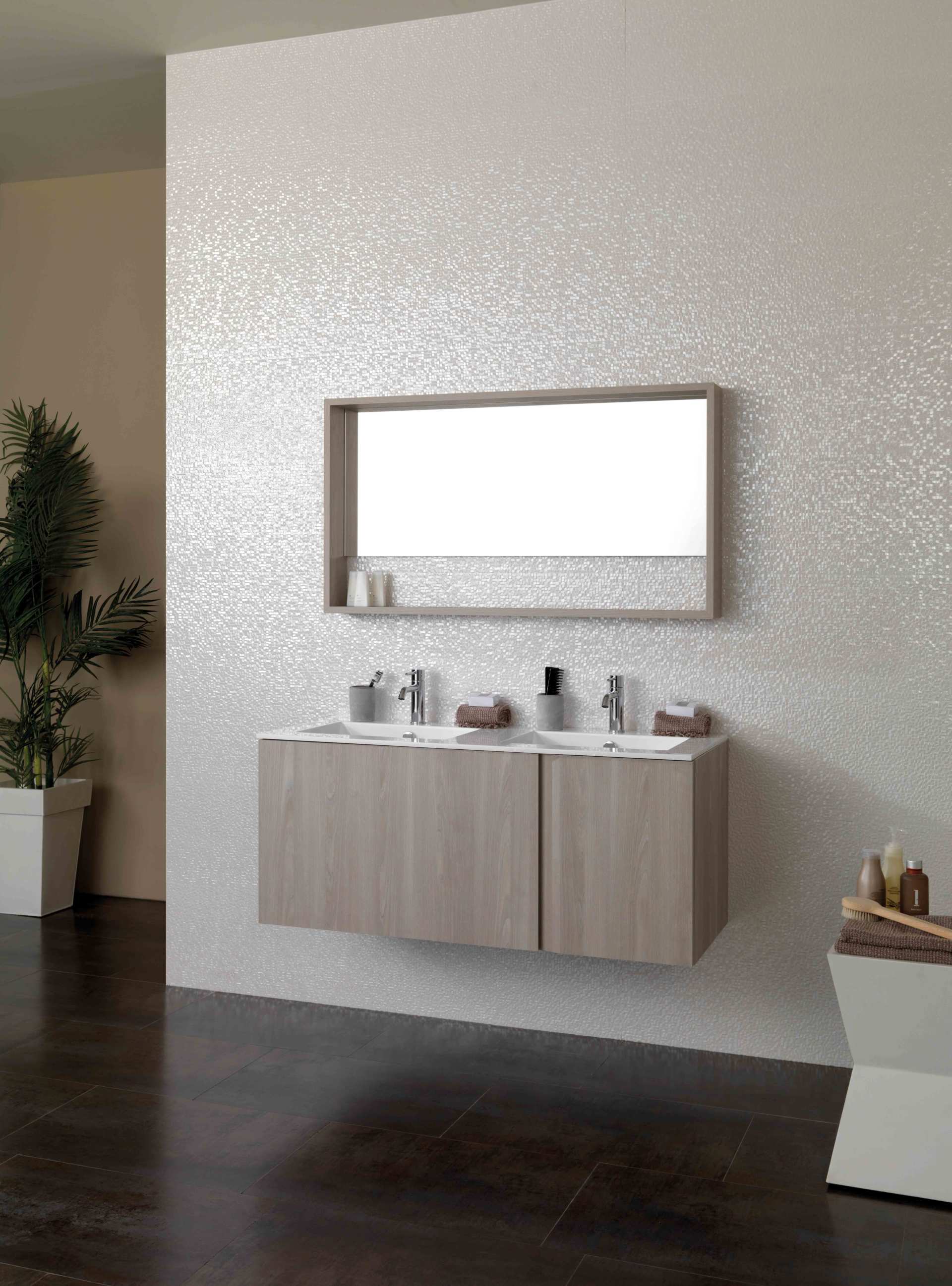 Mobile bagno moderno con specchio, ante in legno chiaro e piano d'appoggio con articoli da bagno, contro una parete con finitura materica.
