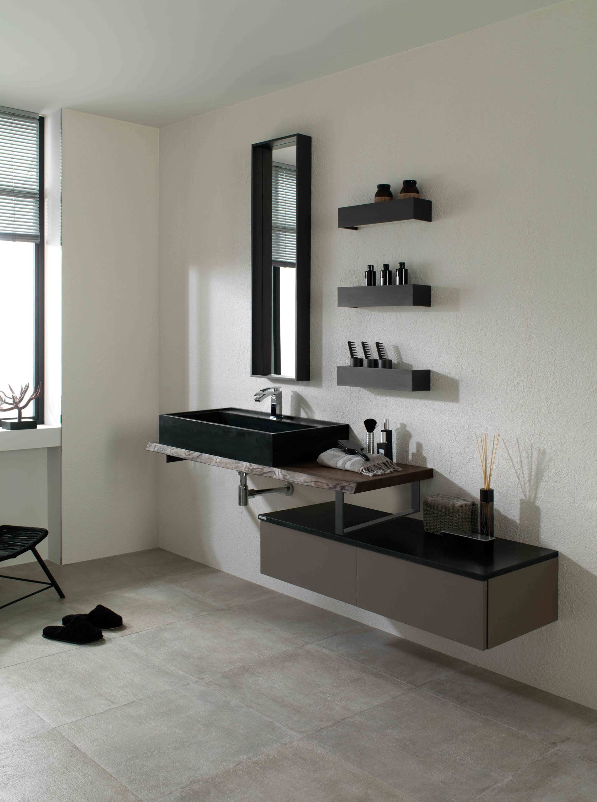 Bagno moderno con lavabo sospeso nero, specchio, mensole e mobiletto grigio su una parete chiara.