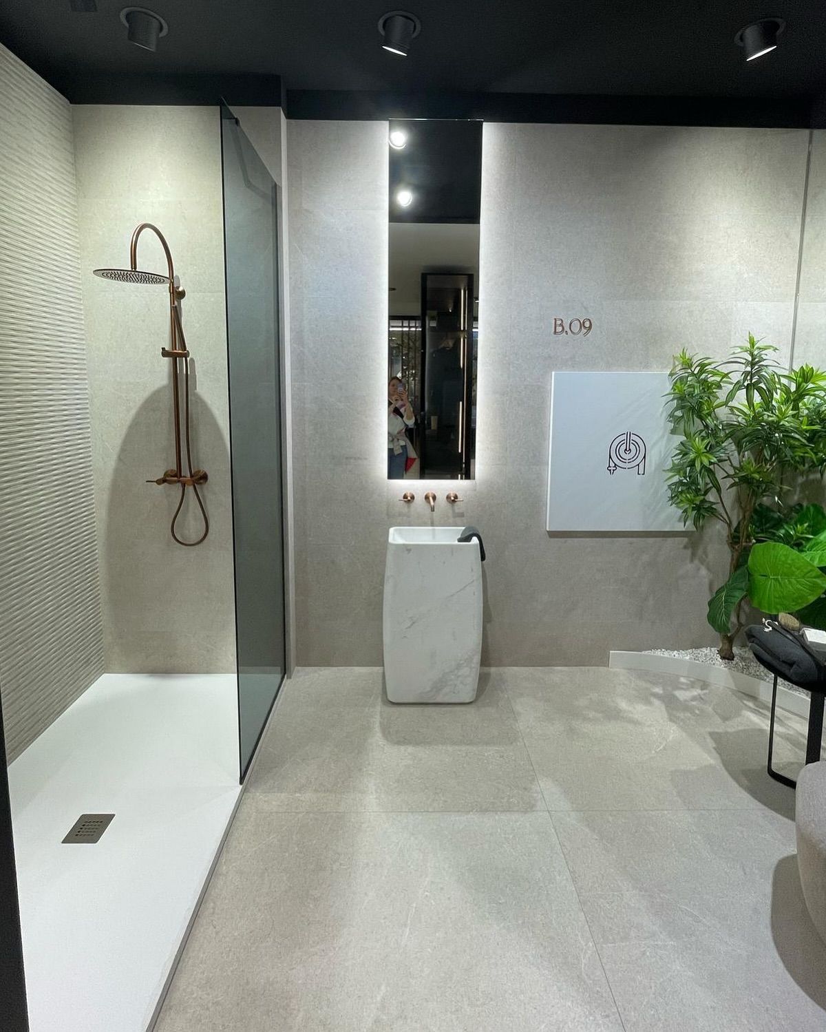 Bagno moderno con piastrelle beige, doccia a parete, lavabo, specchio e pianta in vaso.