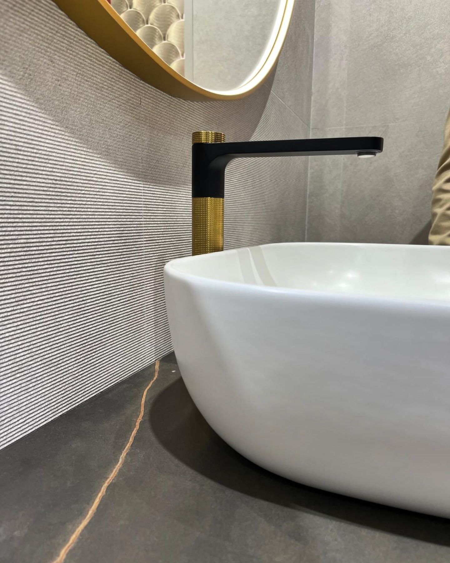 Lavabo moderno con vasca bianca, rubinetto nero e dettagli dorati su piano di lavoro grigio.