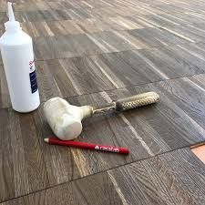 Flacone di colla bianca, rullo per pittura e pennarello rosso su un pavimento con motivo effetto legno.