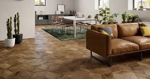 Soggiorno moderno con divano in pelle marrone, pavimento in legno con motivi decorativi, tappeto verde e tavolo da pranzo sullo sfondo.