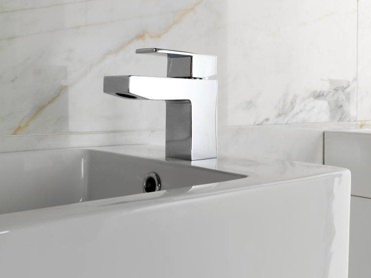 Rubinetto moderno cromato sopra un lavabo bianco da bagno con rivestimento in piastrelle di marmo