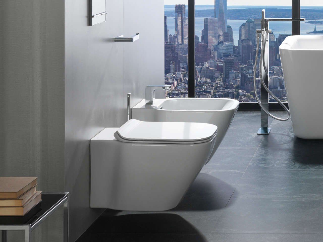 Bagno moderno con WC sospeso, lavabo bianco e vista panoramica sulla città attraverso ampie finestre.