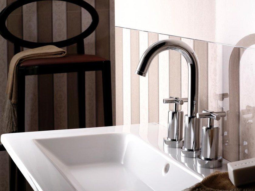 Lavabo bianco con rubinetto cromato accanto a una sedia scura e rivestimento a parete a righe.