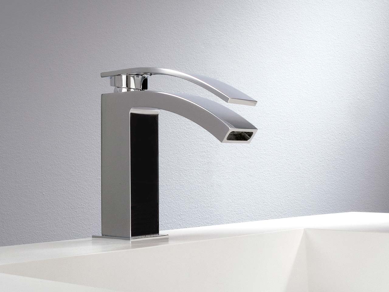 Rubinetto da bagno moderno cromato su lavabo bianco, su una parete grigio chiaro.