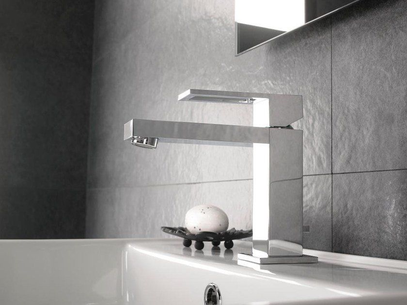Rubinetto da vasca moderno cromato accanto a una vasca bianca, con una parete del bagno rivestita di piastrelle scure sullo sfondo.