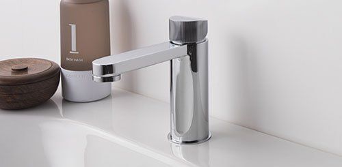 Rubinetto cromato moderno su lavabo bianco da bagno con contenitori marroni e beige nelle vicinanze.