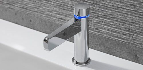 Rubinetto cromato su un lavabo bianco contro una parete piastrellata di grigio.