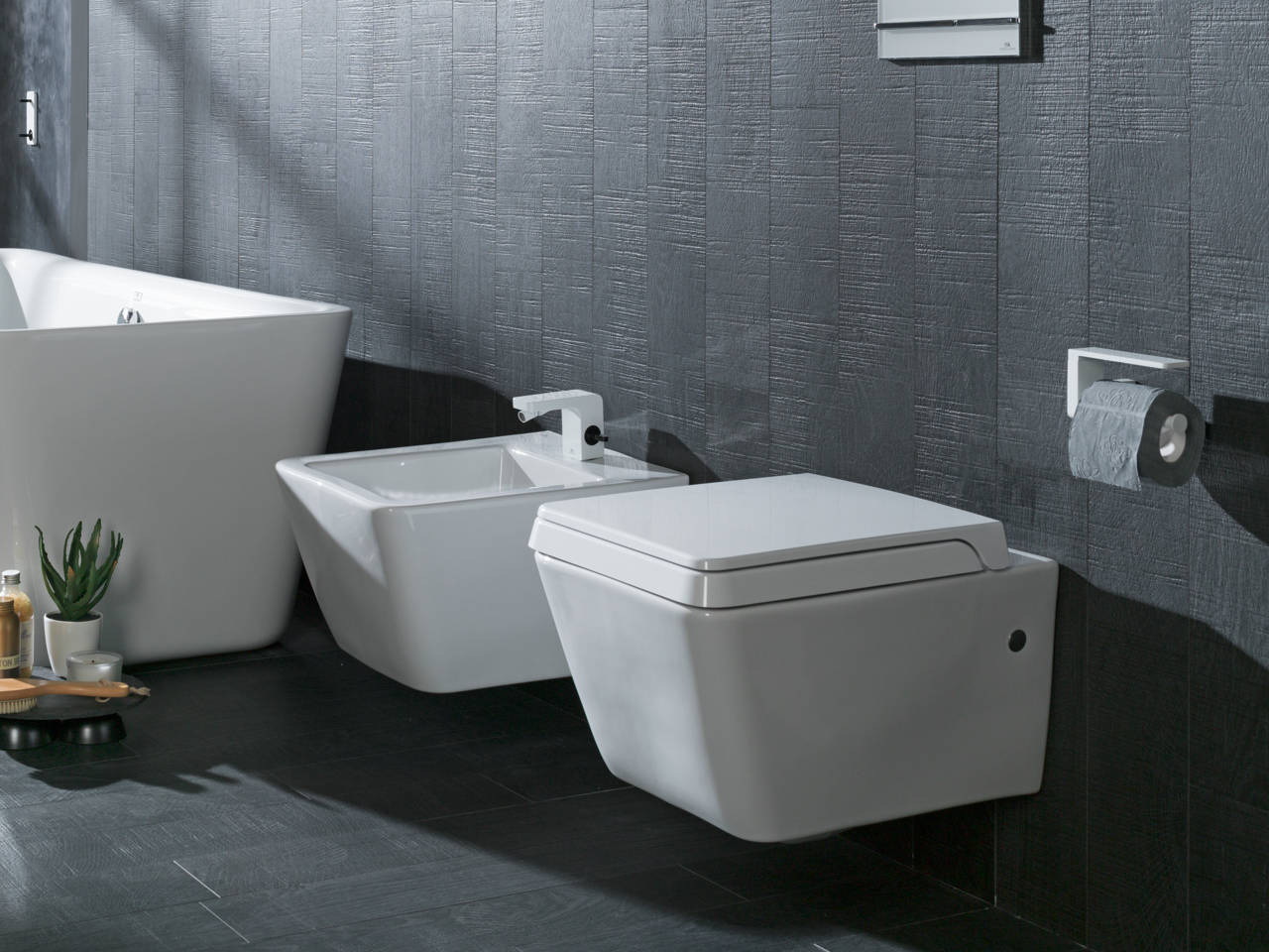 Bagno moderno con WC bianco, bidet e vasca freestanding su piastrelle grigio scuro.