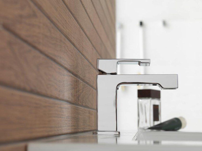 Rubinetto da bagno moderno cromato su un lavabo bianco accanto a una parete rivestita in legno.