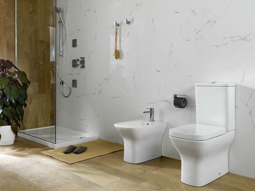 Bagno moderno con WC bianco, bidet, doccia in vetro e dettagli in legno.