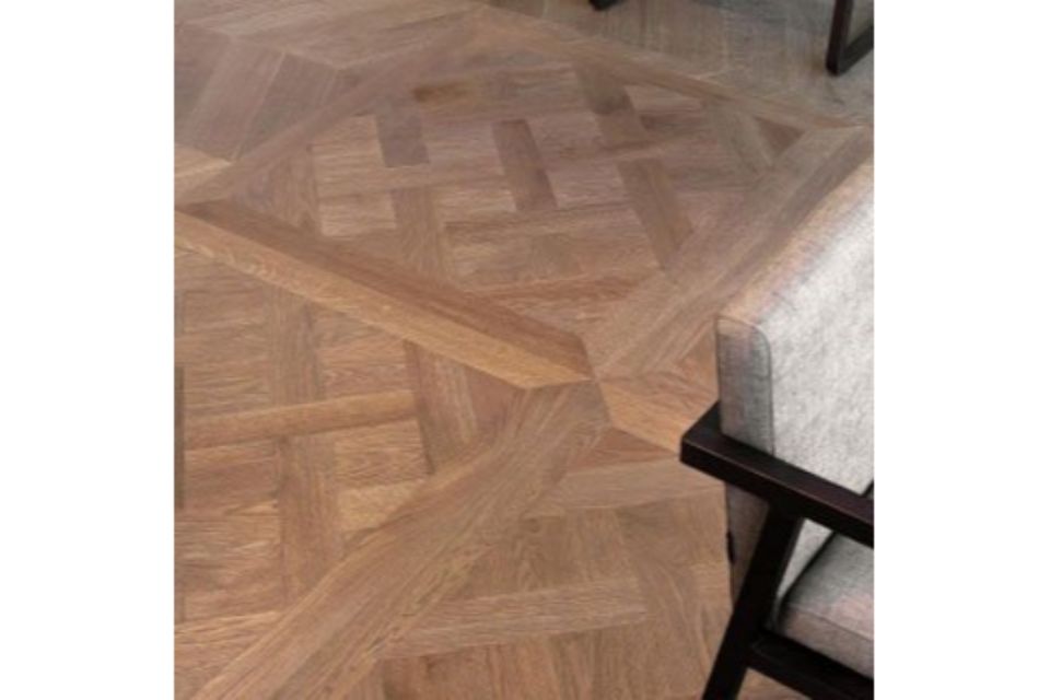 Pavimento in legno a spina di pesce accanto a un divano grigio chiaro con una gamba scura.