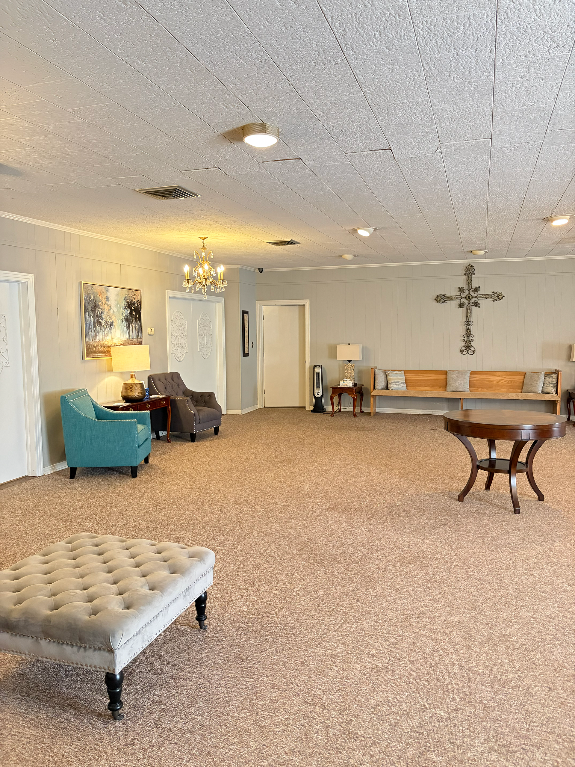 Spacious carpeted lobby with teal chairs, tufted bench, table, and wall art under recessed lighting