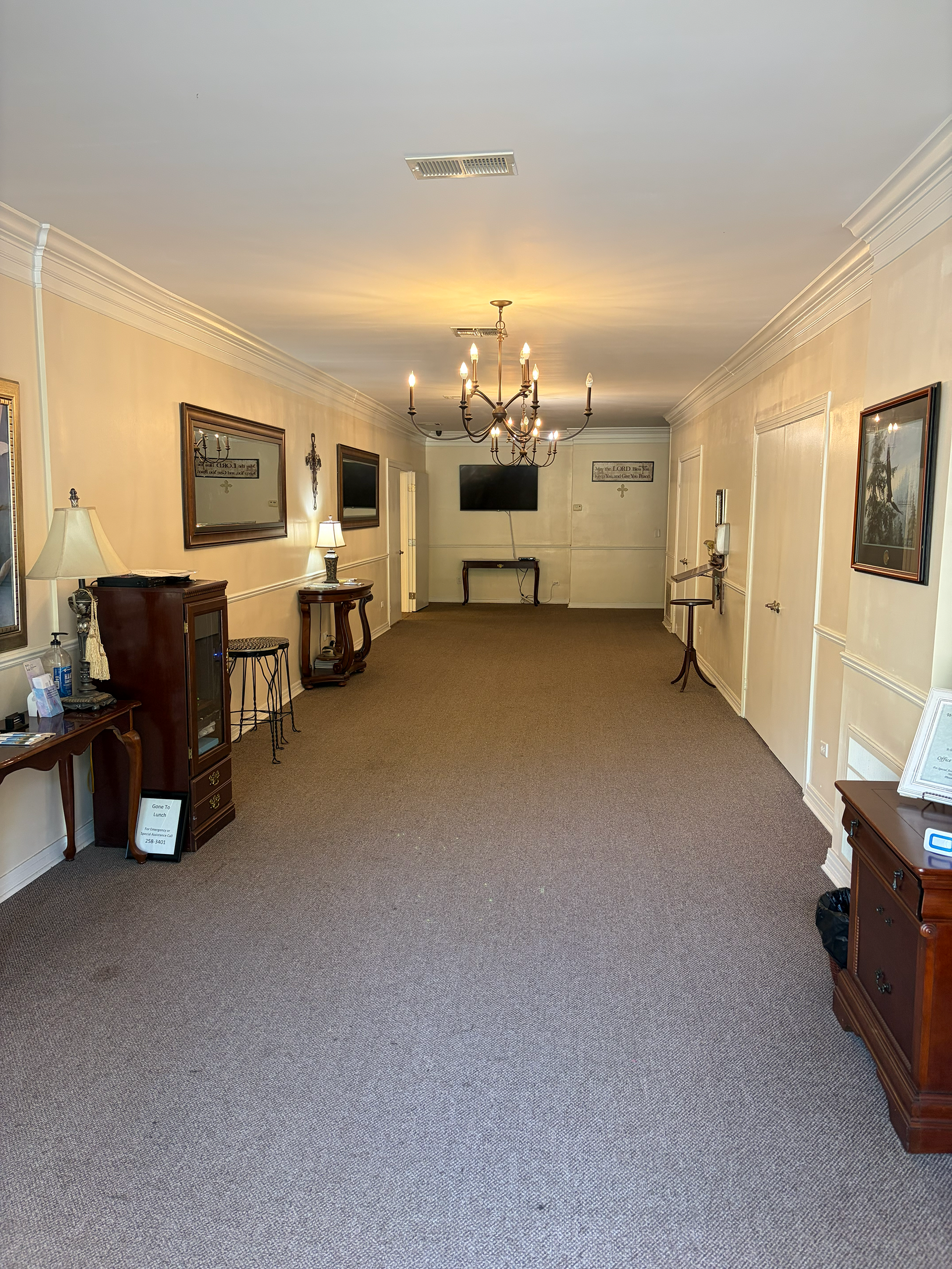 Long carpeted hallway with chandeliers, cream walls, and framed art on both sides