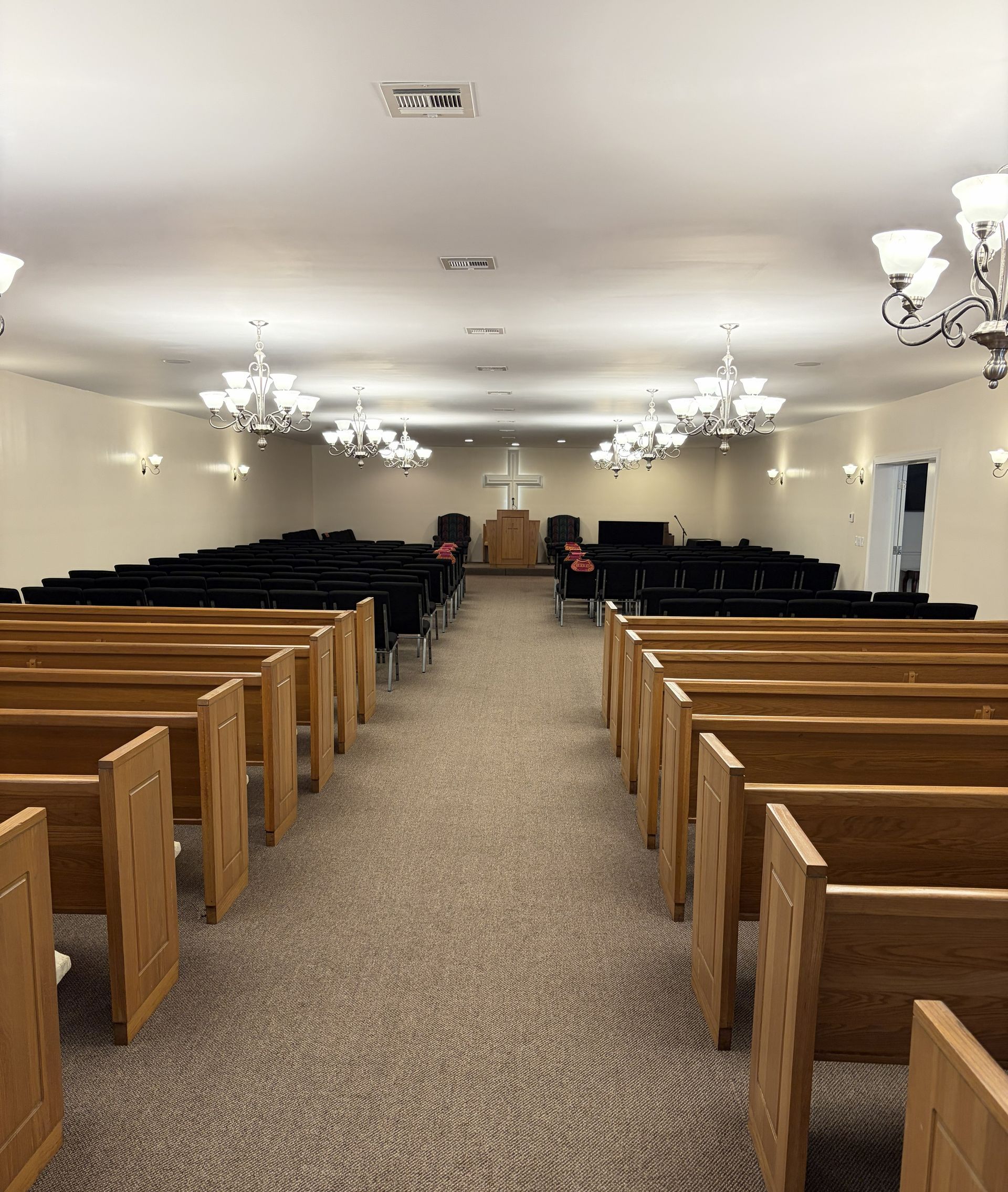 Empty chapel with wooden pews, chandelier lights, and a podium at the front.