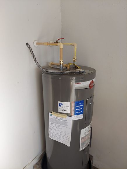A stainless steel water heater is sitting in a corner of a room.