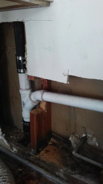 A white pipe is connected to a black pipe in a room.